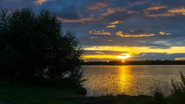 Gölde dramatik bir gün batımı. Gölün kıyısında gün batımı. Yansıma. Mavi gökyüzü ve sarı güneş ışığı. Gün batımında manzara. Panoramik pankart. Doğa konsepti.