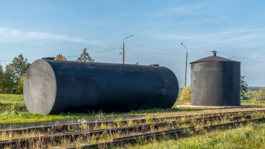 Antika bir demiryolu deposunda metal bir yakıt deposu. Köy tren istasyonunda eski siyah yakıt tankı. Endüstri kavramı.