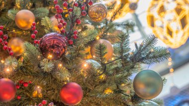 Yılbaşı oyuncağı, top ve arka planda parlayan renkli ışıklarla geleneksel yapay Noel ağacı. Xmas kavramları. Noel ağacına yakın çekim. Odaklanmamış arkaplan.