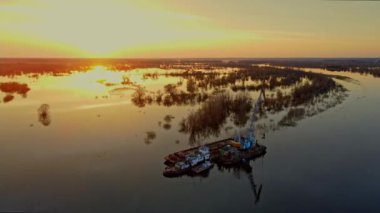 Dredger nehirdeki çim alanını derinleştirmeye çalışıyor. Nehirdeki bir tarakçı tarafından temizleniyor ve derinleşiyor. Nehirde gün batımı. Endüstriyel kavram.