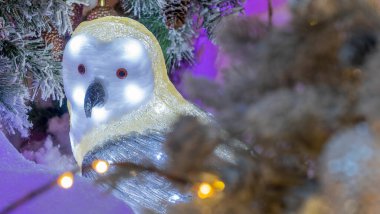 Aydınlatılmış oyuncak baykuş, Noel ağacının arka planında, peri ormanında oturuyor. Yeni yıl konsepti. Odaklanamayan ön plan. Şenlikli dekorasyon.