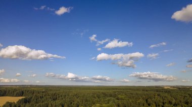 Yeşil tarlalar, orman ve yazın bulutlu mavi gökyüzü. Tarlaları, otları, ağaçları, güneşli gökyüzünü ve yemyeşil yapraklarını içeren soyut bir manzara. İnsansız hava aracıyla manzara.