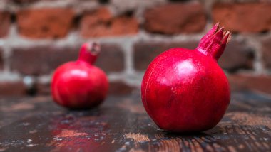 Masada iki kırmızı nar yatıyordu. Kırmızı tuğla duvarlı arka planda masada iki tane olgun taş var. Tüylü yemek. Hayat konsepti.