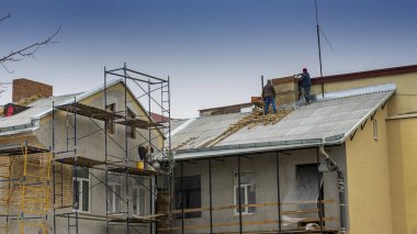 İnşaat işçileri çatıya kiremit döşemişler. İşçi eski binaya yeni çatı kuruyor. Yapı kavramları.