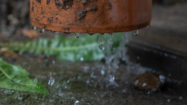 Boru hattından akan yağmur damlalarının yakın görüntüsü. Çatıdan güçlü bir su akışı bir borudan geçer. Yağmur kavramları. Tasarım için resim. Metin için boşluk.
