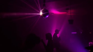 Disko gece kulübünde DJ 'in sahnede yaptığı müzikle dans eden insanların silueti..