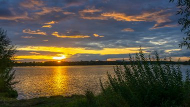 Gölde dramatik bir gün batımı. Gölün kıyısında gün batımı. Yansıma. Mavi gökyüzü ve sarı güneş ışığı. Gün batımında manzara. Panoramik pankart. Doğa konsepti.