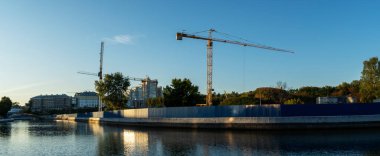 Şehir merkezindeki inşaat alanının panoramik manzarası. Mavi arka planda ağır inşaat malzemelerini kaldırmak için birkaç uzun sarı vinç var. İnşaat endüstrisi. Metin için boşluk.