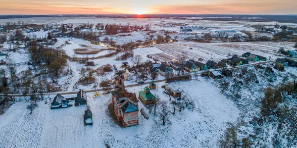 Eski kilise kalıntılarının panoramik manzarası ve günbatımında kar altında modern ahşap şapel. Din kavramı. Kışın kırsal.