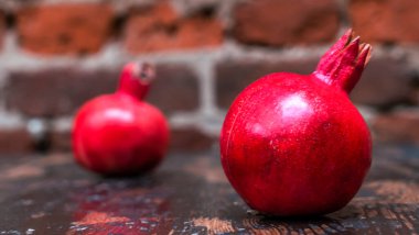 Masada iki kırmızı nar yatıyordu. Kırmızı tuğla duvarlı arka planda masada iki tane olgun taş var. Tüylü yemek. Hayat konsepti.