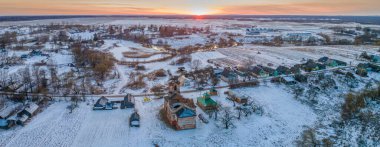 Eski kilise kalıntılarının panoramik manzarası ve günbatımında kar altında modern ahşap şapel. Din kavramı. Kışın kırsal.