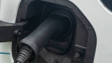Şarj olan bir elektrikli arabaya takılan güç kaynağının yakın görüntüsü. Elektrikli araba şarj oluyor. Arabanın arka tarafı enerji yüklüyor..
