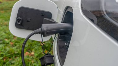 Şarj olan bir elektrikli arabaya takılan güç kaynağının yakın görüntüsü. Elektrikli araba şarj oluyor. Arabanın arka tarafı enerji yüklüyor..