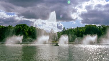 Çeşmeden su. Bulutlu gökyüzünün arkasındaki çeşme akıntısının tepesinde. Nehirdeki çeşme dramatik gökyüzüne karşı. Şehir manzarası görünümü.