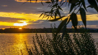 Gölde dramatik bir gün batımı. Gölün kıyısında gün batımı. Yansıma. Mavi gökyüzü ve sarı güneş ışığı. Gün batımında manzara.