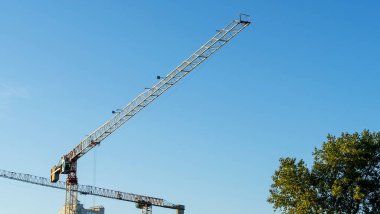 Şehir merkezindeki inşaat alanının panoramik manzarası. Mavi arka planda ağır inşaat malzemelerini kaldırmak için birkaç uzun sarı vinç var. İnşaat endüstrisi. Metin için boşluk.