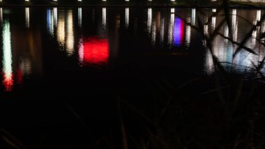 Şehir ışıkları refleksi. Karanlık bir şehir caddesinde çok renkli neon ışıklar, su birikintilerindeki neon ışıklarının yansıması..