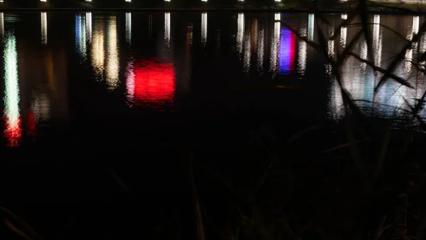 Şehir ışıkları refleksi. Karanlık bir şehir caddesinde çok renkli neon ışıklar, su birikintilerindeki neon ışıklarının yansıması..