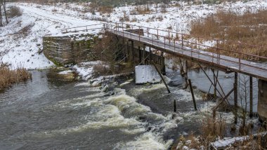 Kış nehri üzerindeki dar eski ahşap köprü. Kırsal kesimdeki nehir üzerinde tahta yaya köprüsü. Kış manzarası. Doğa kavramları.