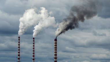 Gökyüzü arka planında bacadan çıkan endüstriyel duman. Kömür santralinden çıkan gri dumanlı yüksek baca borularının görüntüsü. Fosil yakıtlı elektrik üretimi. Rüzgâr kirliliği.