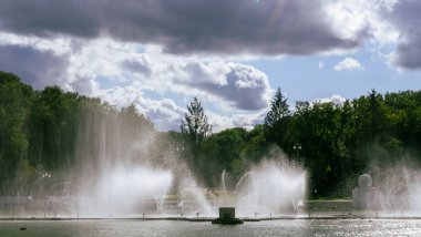 Çeşmeden su. Bulutlu gökyüzünün arkasındaki çeşme akıntısının tepesinde. Nehirdeki çeşme dramatik gökyüzüne karşı. Şehir manzarası görünümü.