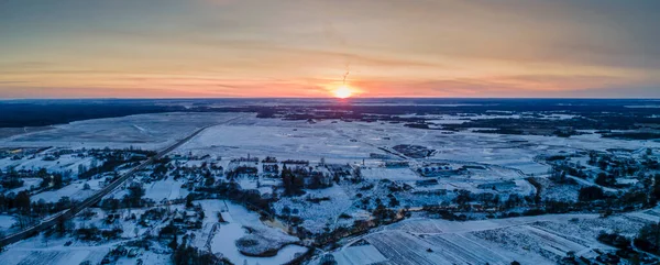 Panoramic view of red sunset in a winter evening over a village and field.