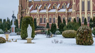 Kış çimenliği, köyde thuja ağaçları ve park heykelleri var. Peyzaj tasarımı. Bahçe kavramları. Arka planda eski bir kilise var..