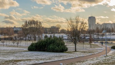 İlk kar şehirdeki yerleşim yerlerini kaplıyor. Güneş ışığı ve bulutlu gökyüzü. Şehir kavramları. Arka planda yüksek binalar var..