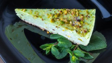 Siyah tabakta nane yaprağı olan yeşil şam fıstıklı kekin yakın görüntüsü. Kremalı fıstıklı cheesecake. Kutlama kavramları.