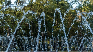 Bir sürü küçük su püskürtüsü olan halka açık bir çeşmenin yakın görüntüsü. Kavisli ışık çizgileri ve parlak su damlalarıyla soyut doğal görüntü. Kamu parkı geçmişi.