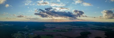 Yeşil tarlalar, orman ve yazın bulutlu mavi gökyüzü. Tarlaları, otları, ağaçları, güneşli gökyüzünü ve yemyeşil yapraklarını içeren soyut bir manzara. İnsansız hava aracıyla manzara.