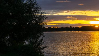 Gölde dramatik bir gün batımı. Gölün kıyısında gün batımı. Yansıma. Mavi gökyüzü ve sarı güneş ışığı. Gün batımında manzara. Panoramik pankart. Doğa konsepti.