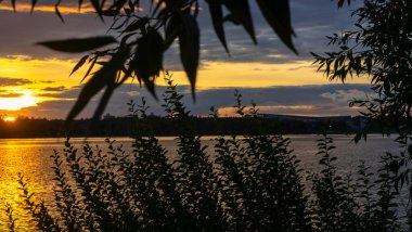 Göldeki şafak güneşinin ışınları. Nehirdeki günbatımı bulutlarının yansıması. Kırsal alan. Panoramik pankart.