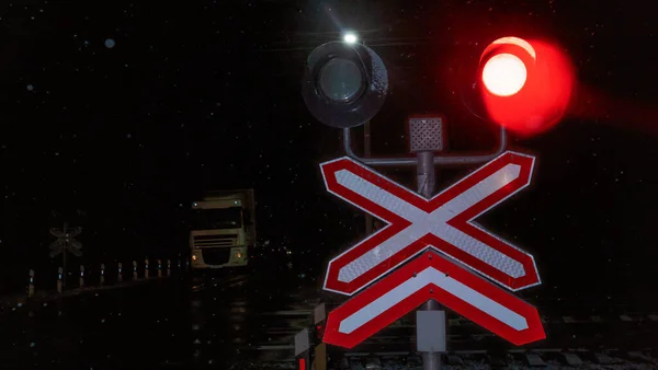 Train crossing gates closed at night. Train grade crossing with blinking or flashing lights while train is moving past. Safety concept.