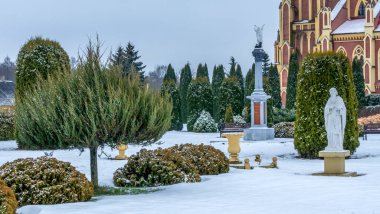 Kış çimenliği, köyde thuja ağaçları ve park heykelleri var. Peyzaj tasarımı. Bahçe kavramları. Arka planda eski bir kilise var..