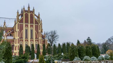 Kış çimenliği, köyde thuja ağaçları ve park heykelleri var. Peyzaj tasarımı. Bahçe kavramları. Arka planda eski bir kilise var..