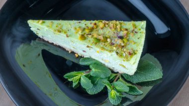Siyah tabakta nane yaprağı olan yeşil şam fıstıklı kekin yakın görüntüsü. Kremalı fıstıklı cheesecake. Kutlama kavramları.