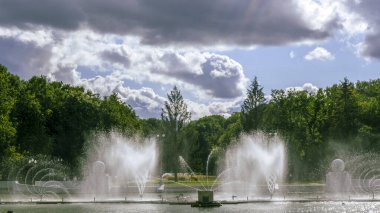 Çeşmeden su. Bulutlu gökyüzünün arkasındaki çeşme akıntısının tepesinde. Nehirdeki çeşme dramatik gökyüzüne karşı. Şehir manzarası görünümü.