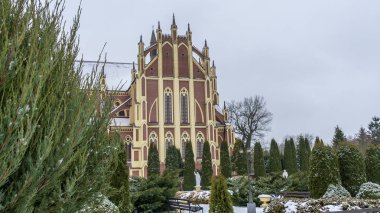 Kış çimenliği, köyde thuja ağaçları ve park heykelleri var. Peyzaj tasarımı. Bahçe kavramları. Arka planda eski bir kilise var..