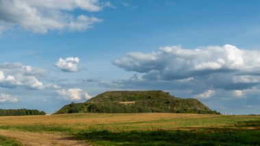 Kapalı şehir çöplüğü. Bölgenin restorasyonu. Büyük bir çöp yığınının peyzajı. Arka planda bir metropol ve bulutlu mavi bir gökyüzü var..