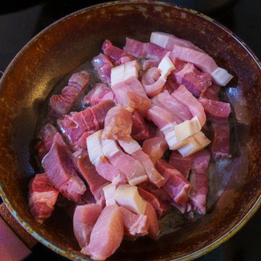 Domuz pastırması kızartma tavasında pişiriliyor. Çiğ kırmızı pastırma.