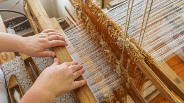 Weaving and manufacturing of handmade fabric close up. Womens hands behind a loom make cloth. Traditional concept.