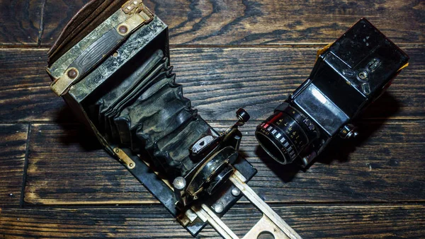 Two antique old photo cameras on the wooden background. History of photography concept.