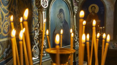 Blurred wax burning candles in an orthodox church on the icon background.