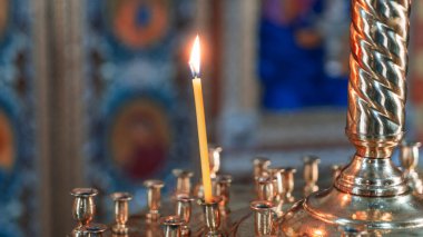Wax burning candle in an orthodox church on the icon background.