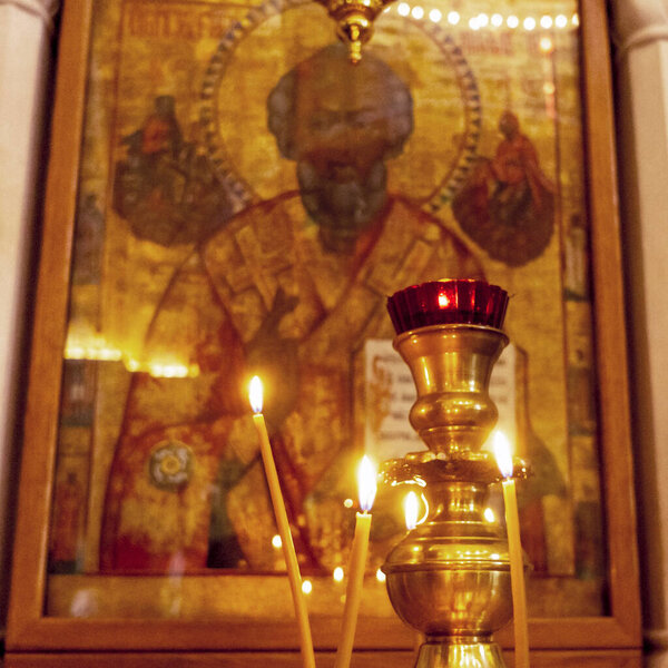 Wax burning candles in an orthodox church on the icon background.