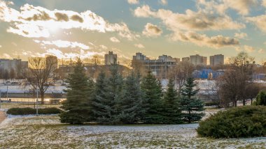 İlk kar şehirdeki yerleşim yerlerini kaplıyor. Güneş ışığı ve bulutlu gökyüzü. Şehir kavramları. Arka planda yüksek binalar var..