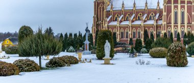 Kış çimenliği, köyde thuja ağaçları ve park heykelleri var. Peyzaj tasarımı. Bahçe kavramları. Arka planda eski bir kilise var..
