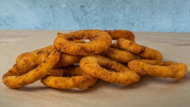 Bar menüsü için yakın plan görüntü. Sulu çıtır soğan halkaları maydanoz yapraklı bir zanaat zemininde yatıyor. Tabağın adı için boşluk.