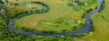 Yeşil tarladaki kıvrımlı nehrin havadan manzarası, insansız hava aracının güzel doğa arka planının üst görüntüsü. Kopya alanı olan mevsimlik yaz manzarası.